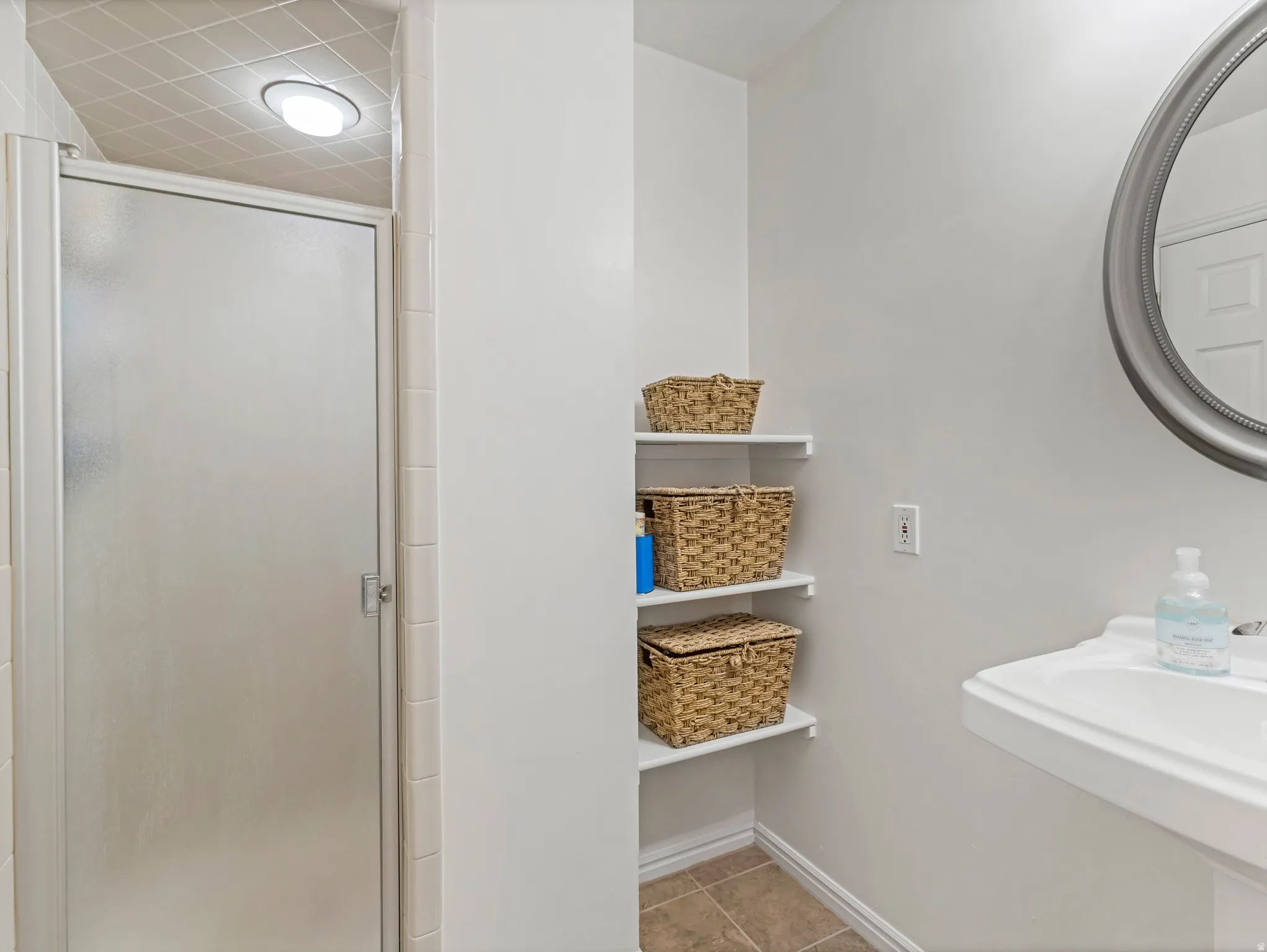 Bathroom with a wall-mounted sink, an oval mirror, and a shower enclosure featuring a frosted glass door
