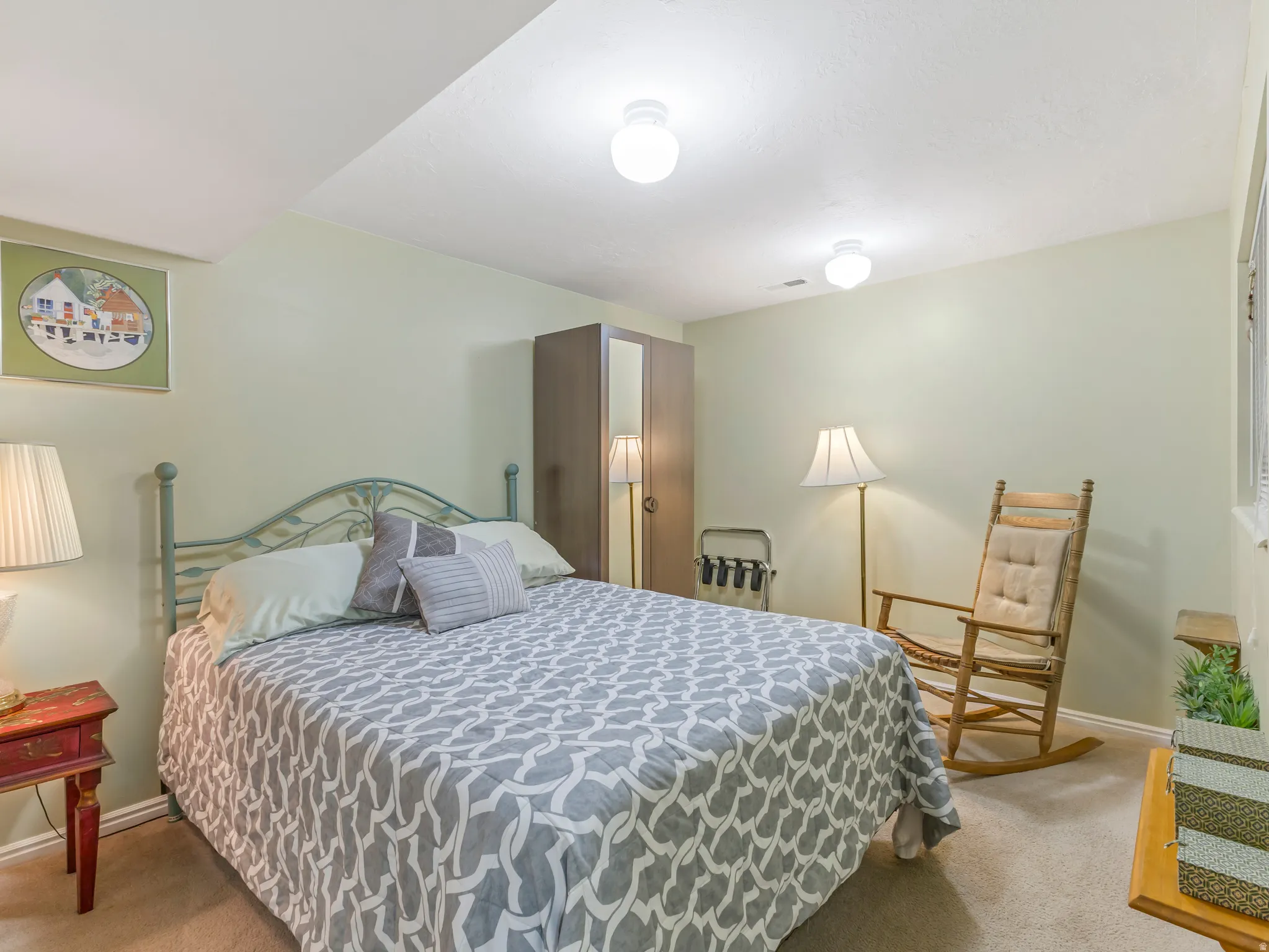 Carpeted room with light green walls, featuring a bed with an ornate metal headboard, a built-in wardrobe, and ceiling-mounted light fixtures