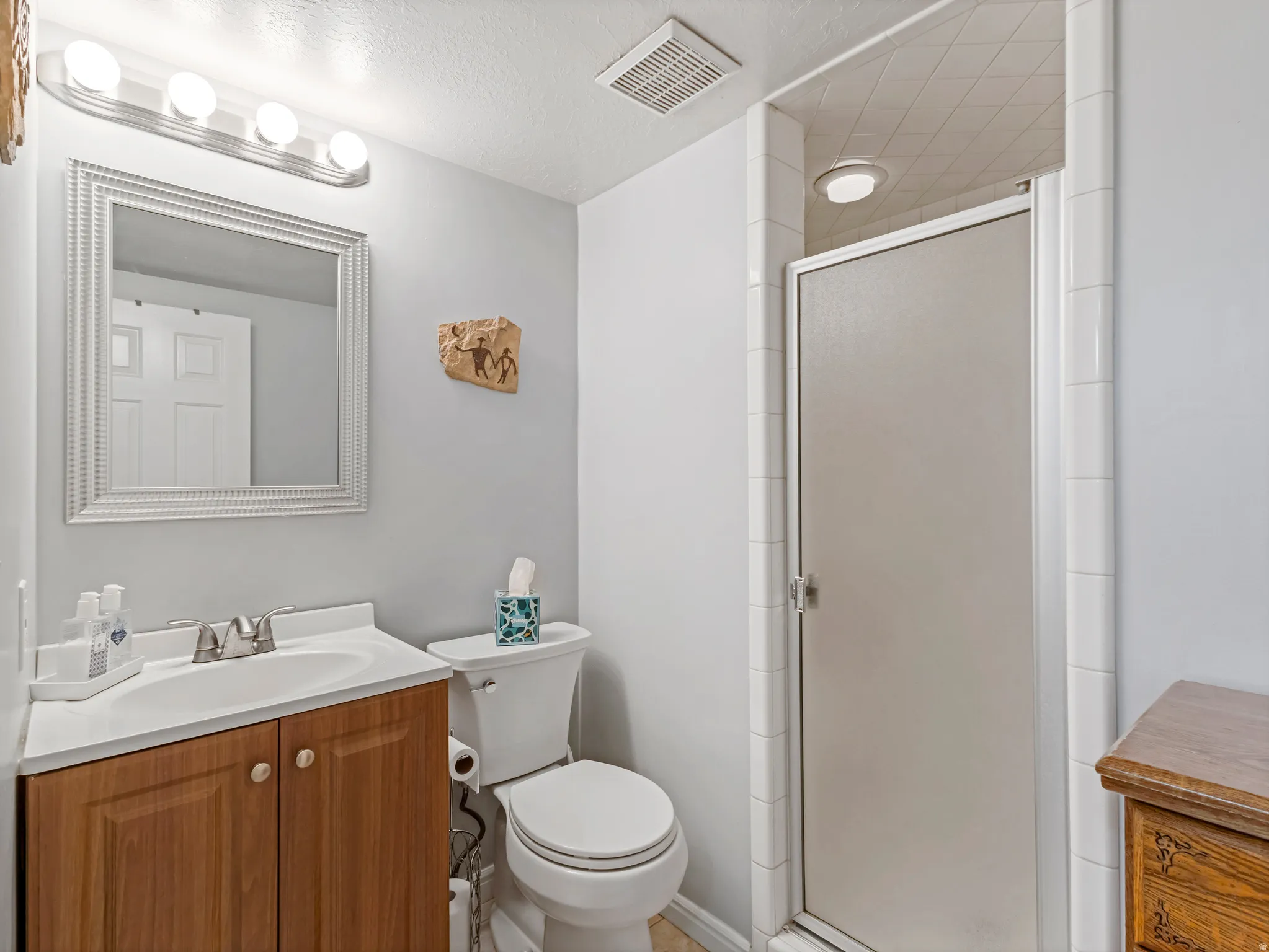 Full bathroom featuring a wood-finish vanity with an integrated sink, a white toilet, and a stand-up shower with a frosted glass door
