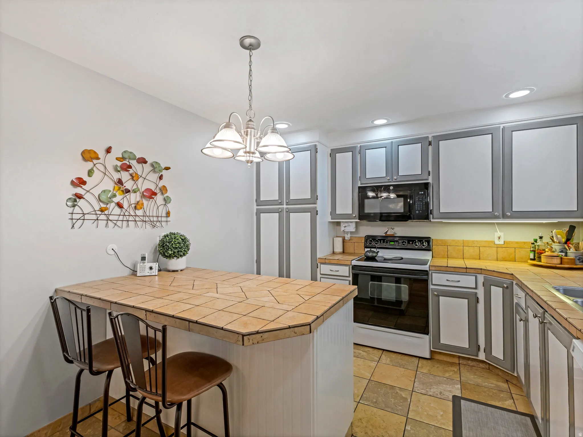 Kitchen featuring an eat-at peninsula with a tile surface, extensive cabinetry with gray trim, a built-in microwave, and a black and white range