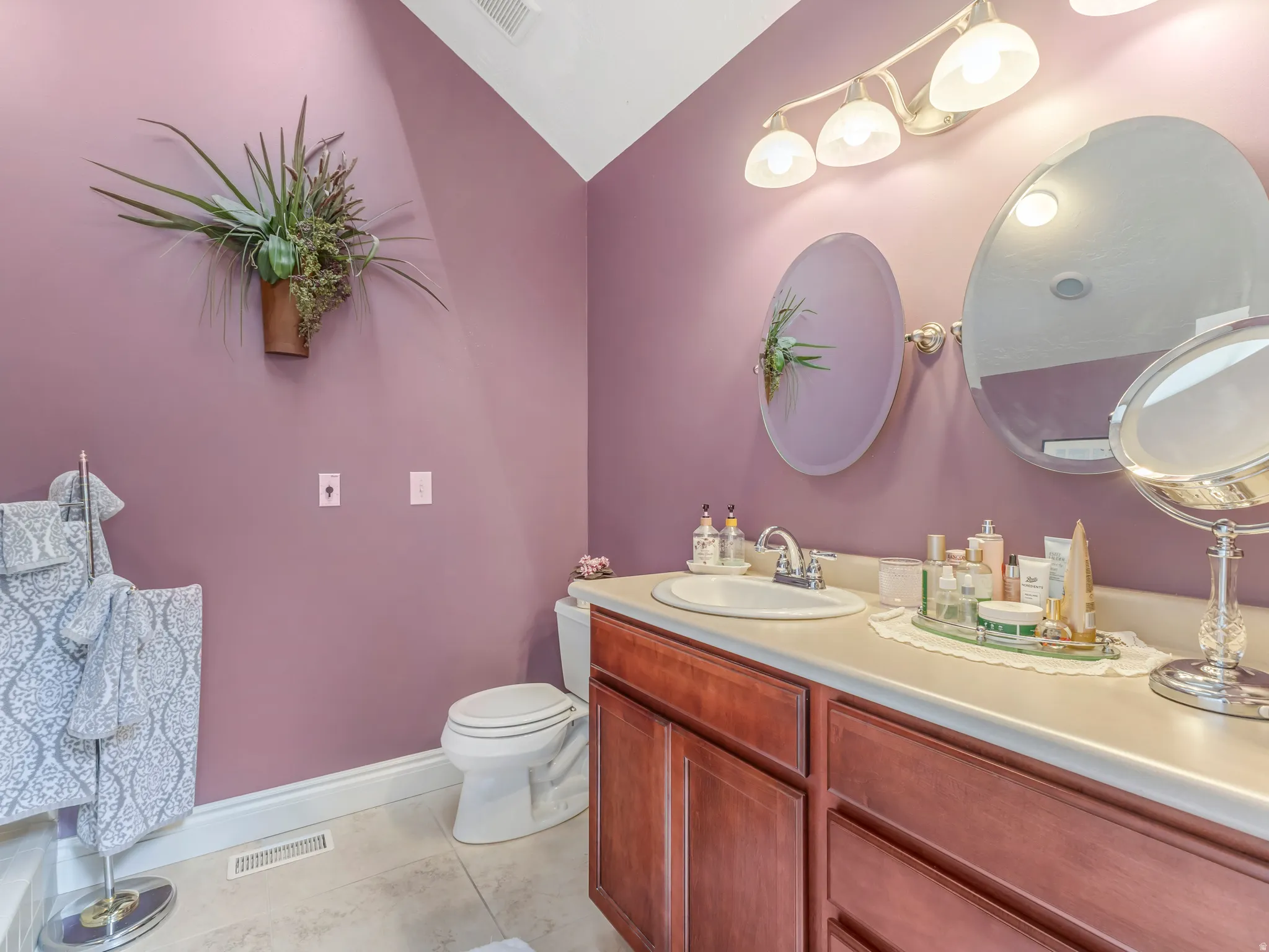 Vanity area featuring a single basin sink, wood-finish cabinetry, light-toned countertop, and two wall-mounted oval mirrors