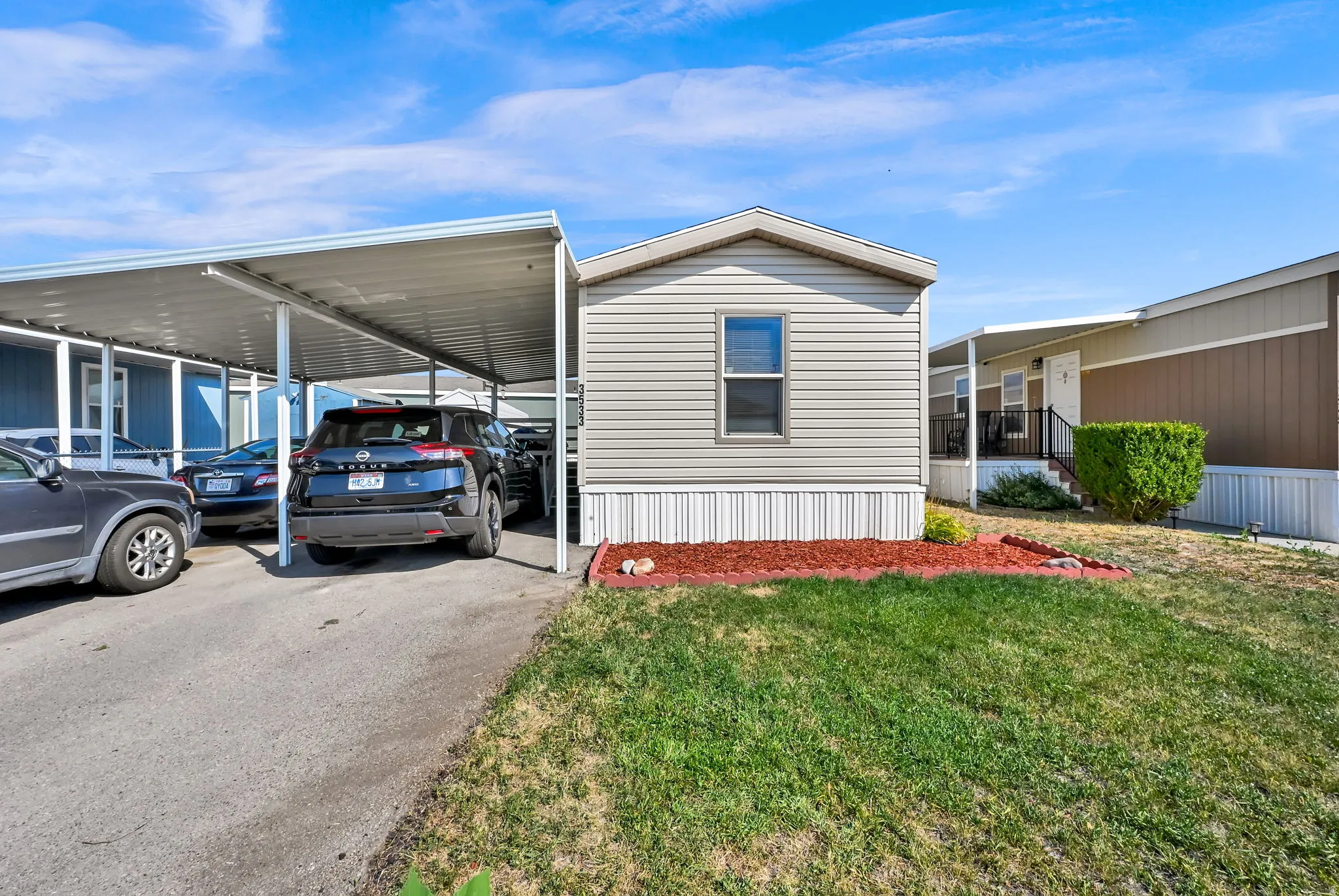Siding exterior with a covered carport, paved driveway, and manicured lawn