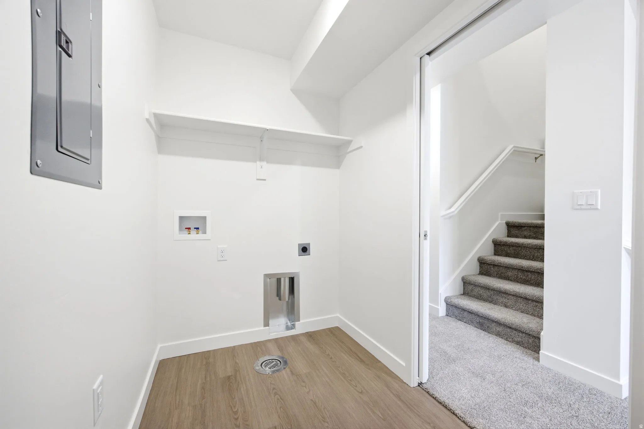 Dedicated laundry area with wood-finish flooring, white shelving, and a floor drain