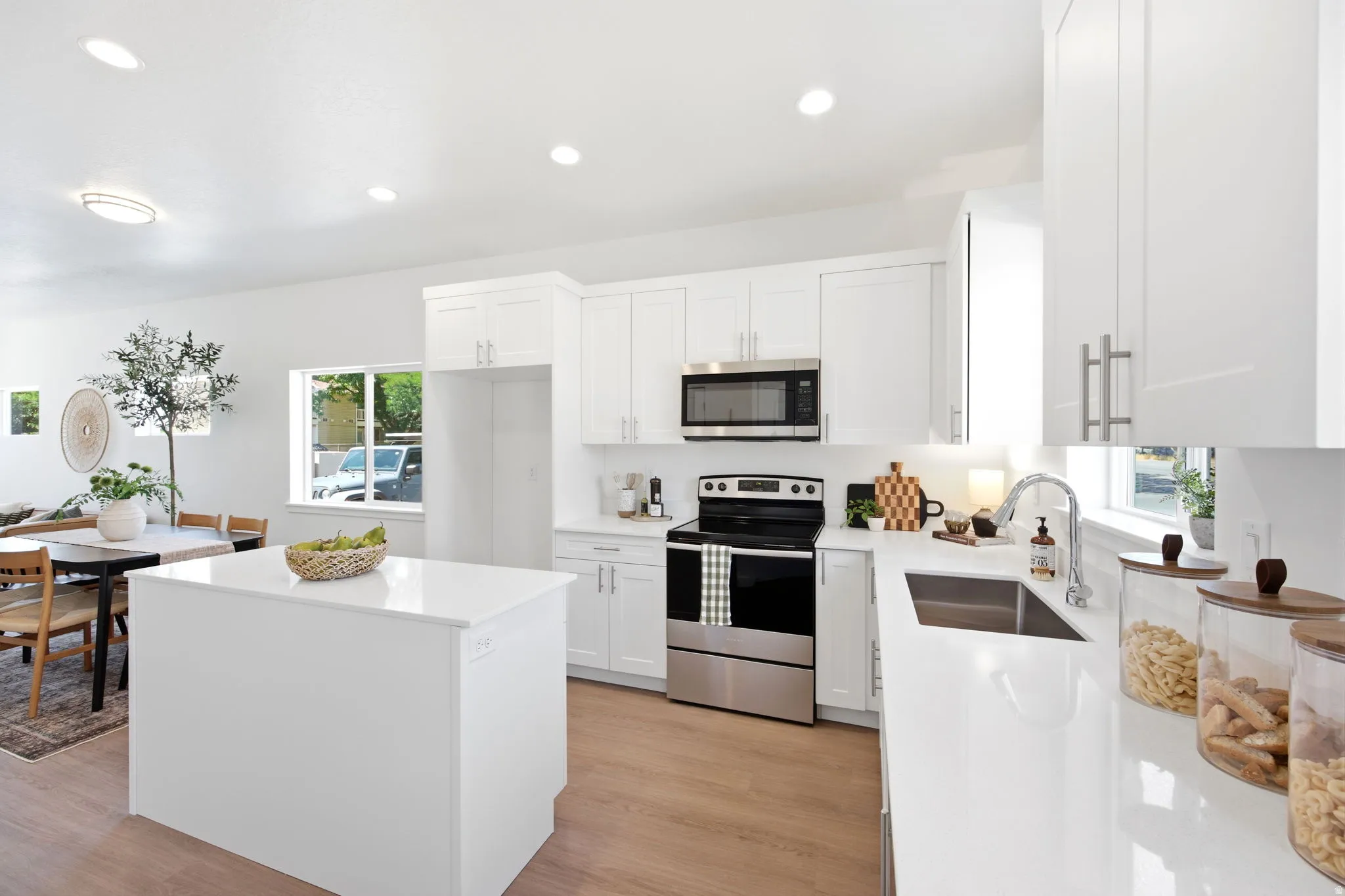 Contemporary kitchen featuring white cabinetry, light countertops, wood-finish flooring, a stainless steel microwave, and a stainless steel range