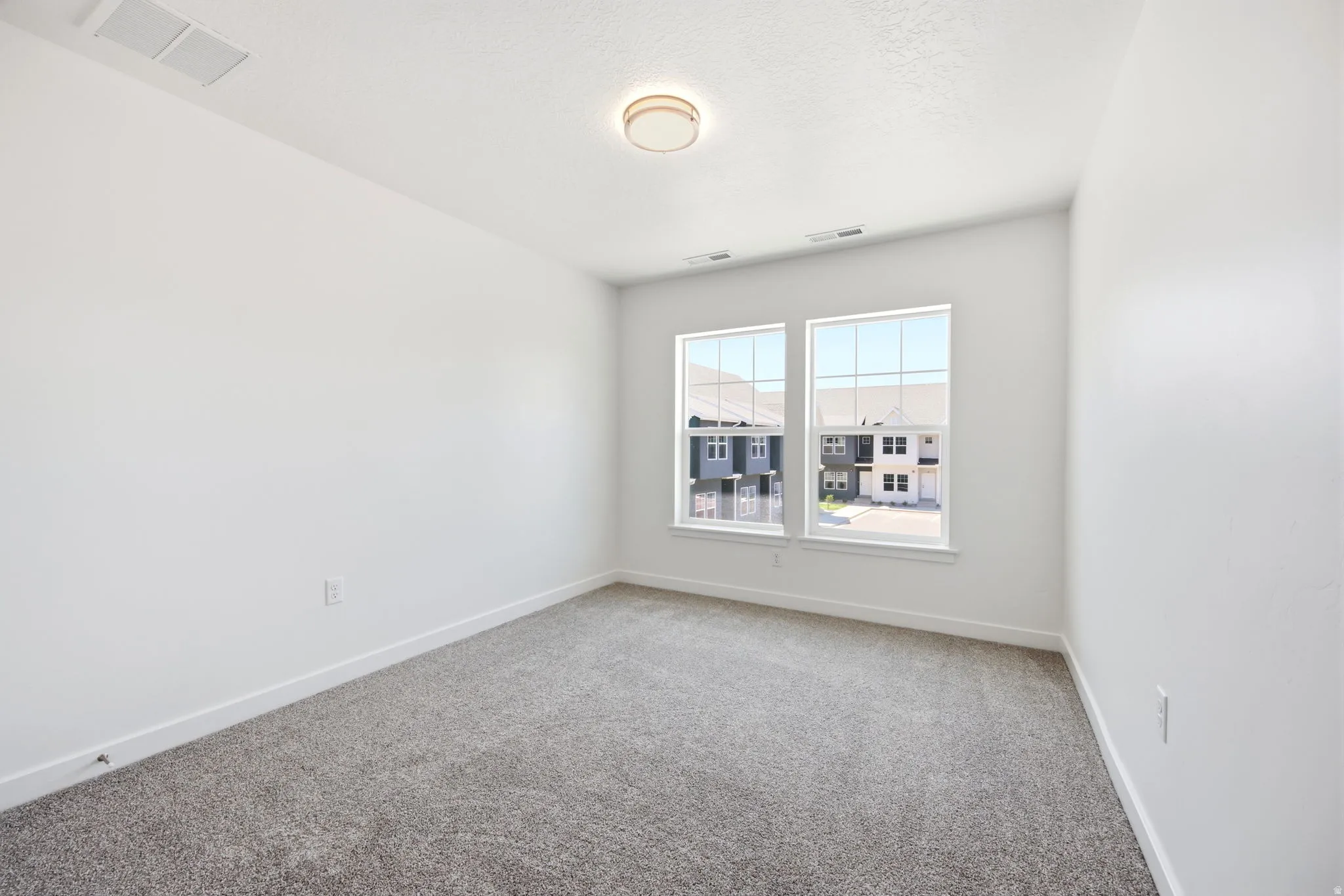Bright room featuring two large windows, neutral gray carpet, white walls, white trim, and a contemporary ceiling light fixture