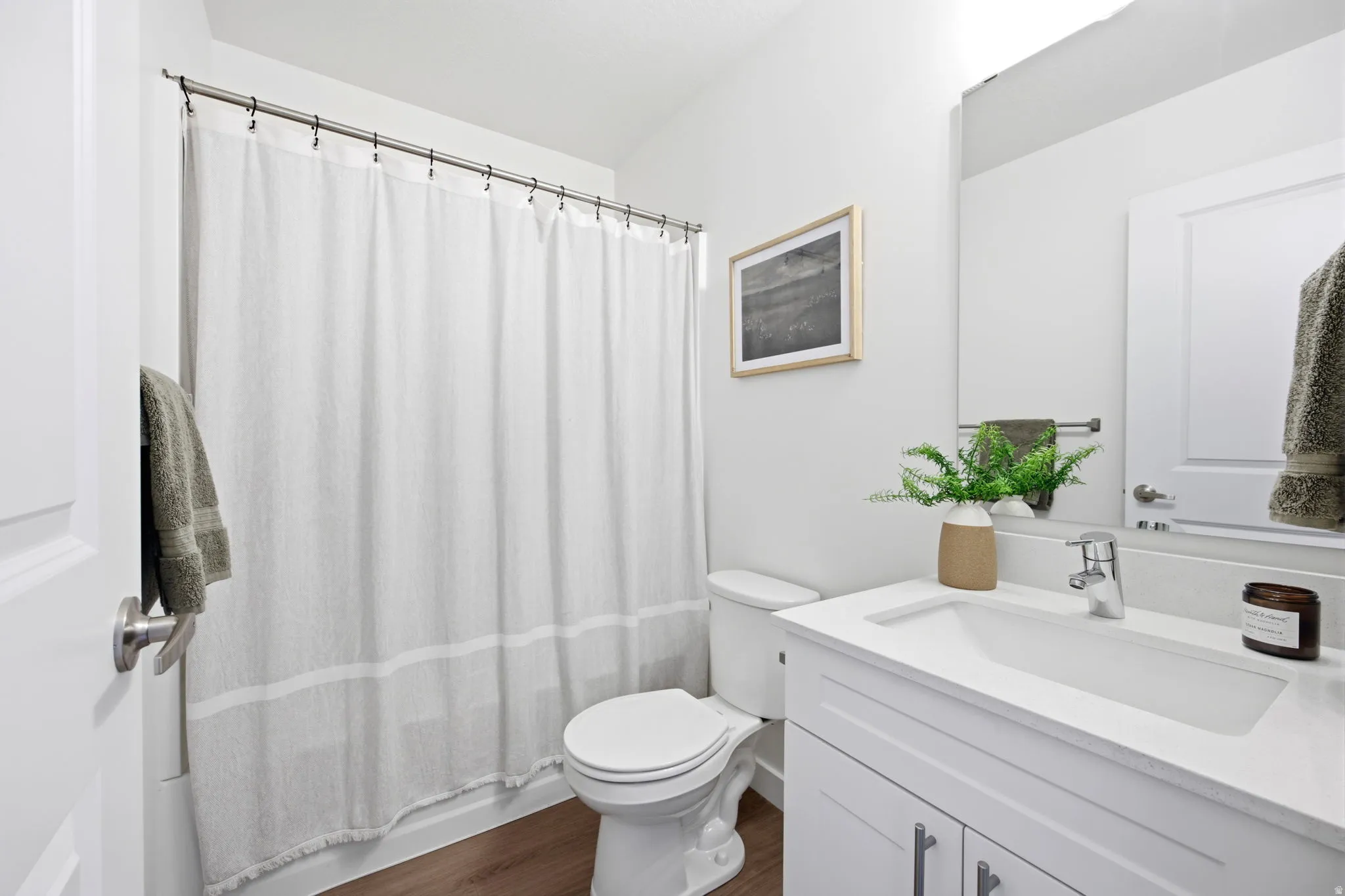Bathroom featuring a white vanity with integrated sink, chrome faucet, wall-mounted mirror, and wood-finish flooring