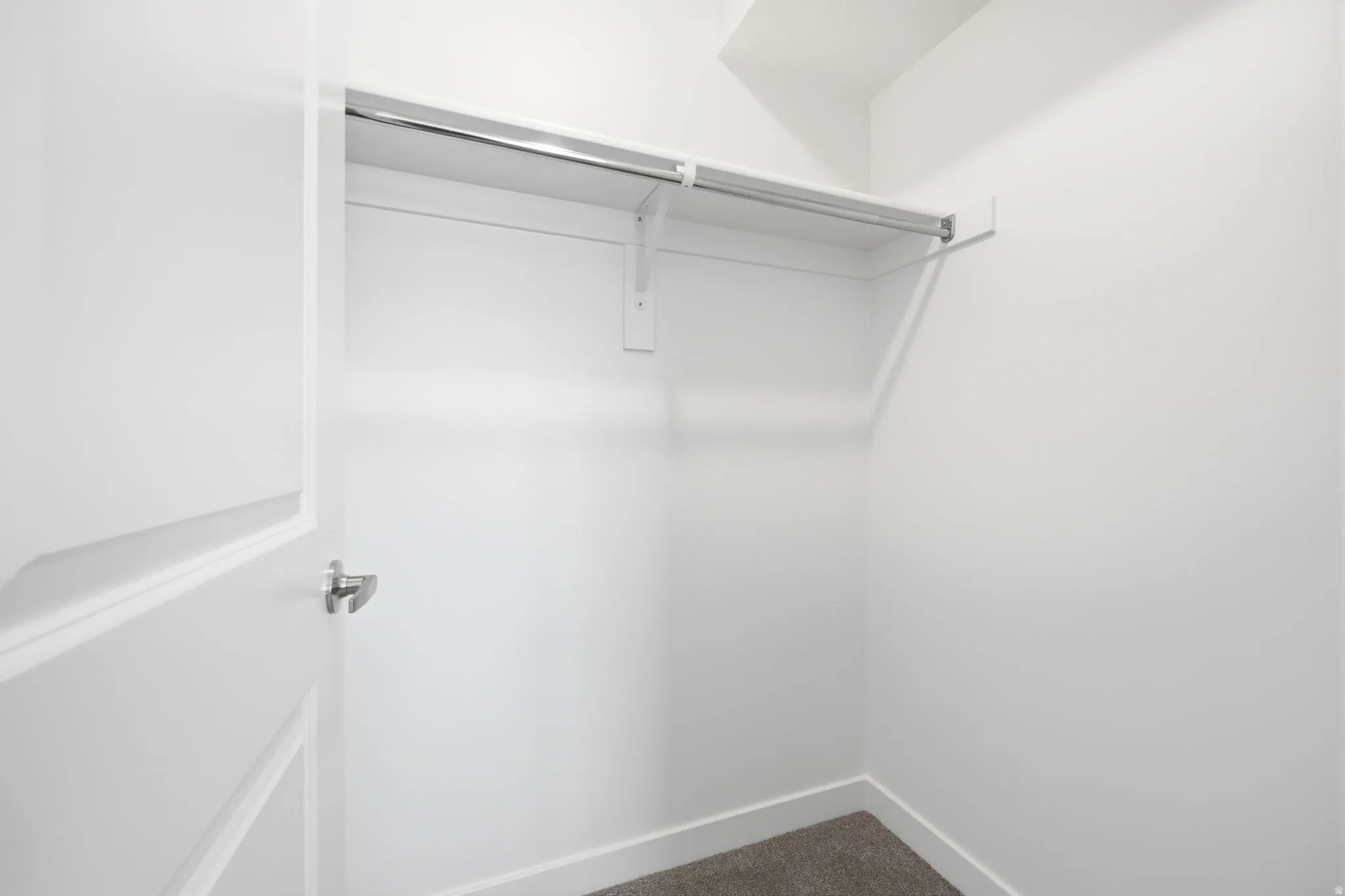 Spacious closet featuring a white door, white walls, and a single clothing rod with an upper shelf