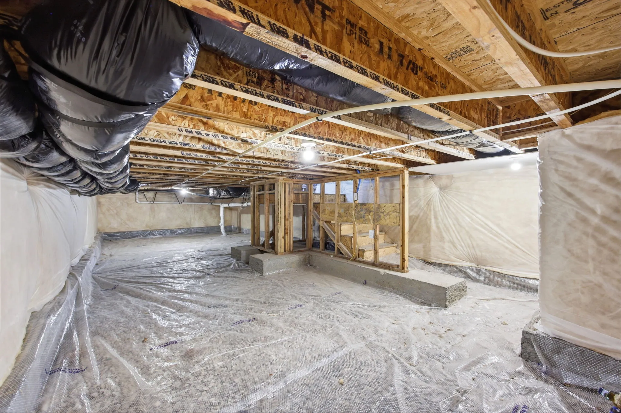 Crawl space with wood framing, exposed joists, and a vapor barrier covering the floor and walls
