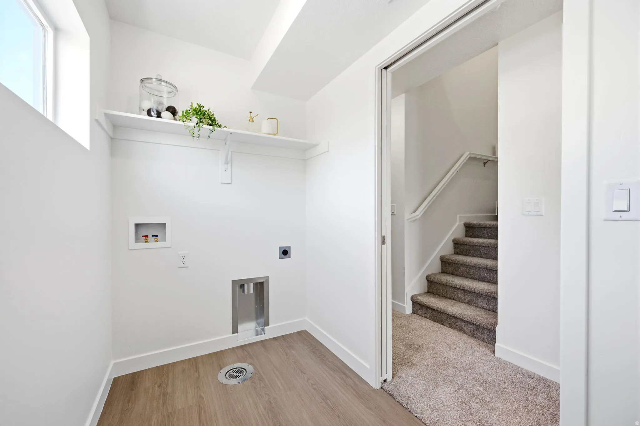 Dedicated laundry area featuring wood-finish flooring, a wall-mounted shelf, and a utility sink drain