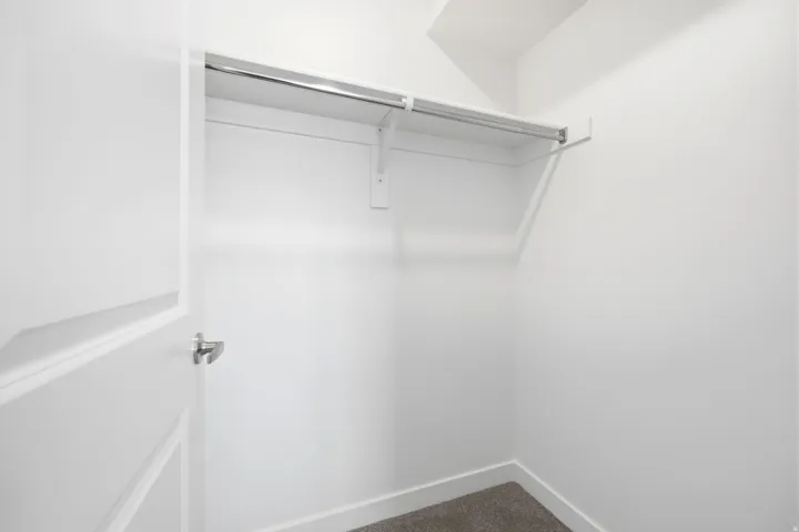 Spacious closet featuring a white door, white walls, and a single clothing rod with an upper shelf