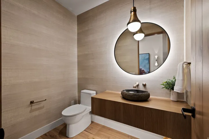 Powder room featuring wood-finish flooring, a contemporary vanity with a stone vessel sink, and an illuminated irregular-shaped mirror