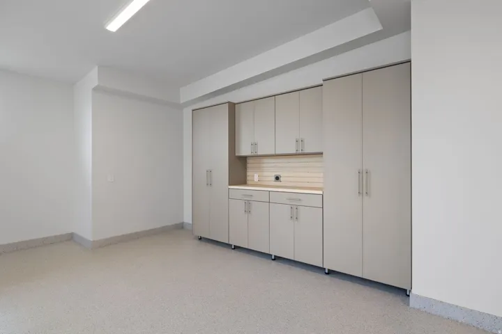 Garage featuring extensive built-in cabinetry, durable epoxy flooring, an integrated workbench, overhead lighting, and abundant storage