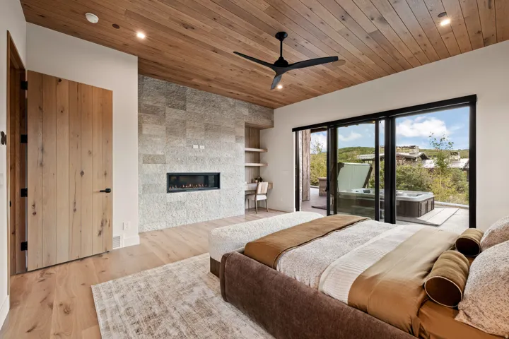 Bedroom featuring a wood-panel ceiling, stone accent wall with a linear fireplace, and wood-finish flooring