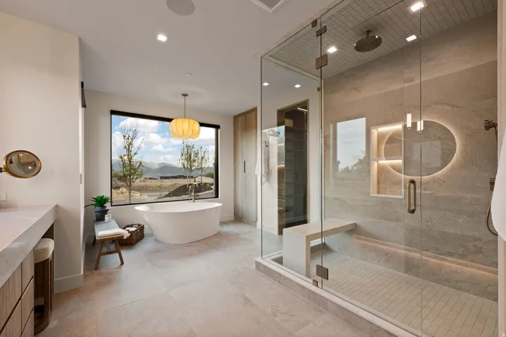 Spacious bathroom featuring a freestanding soaking tub under a large picture window, a large walk-in shower with a built-in bench, a custom stone-finish vanity, and integrated recessed lighting
