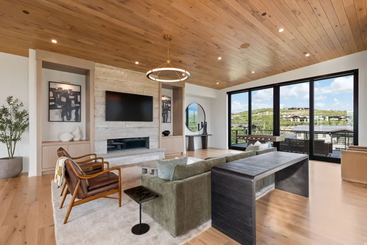 Spacious living area featuring a wood-panel ceiling, light wood-finish flooring, and a stone-clad fireplace with a linear insert