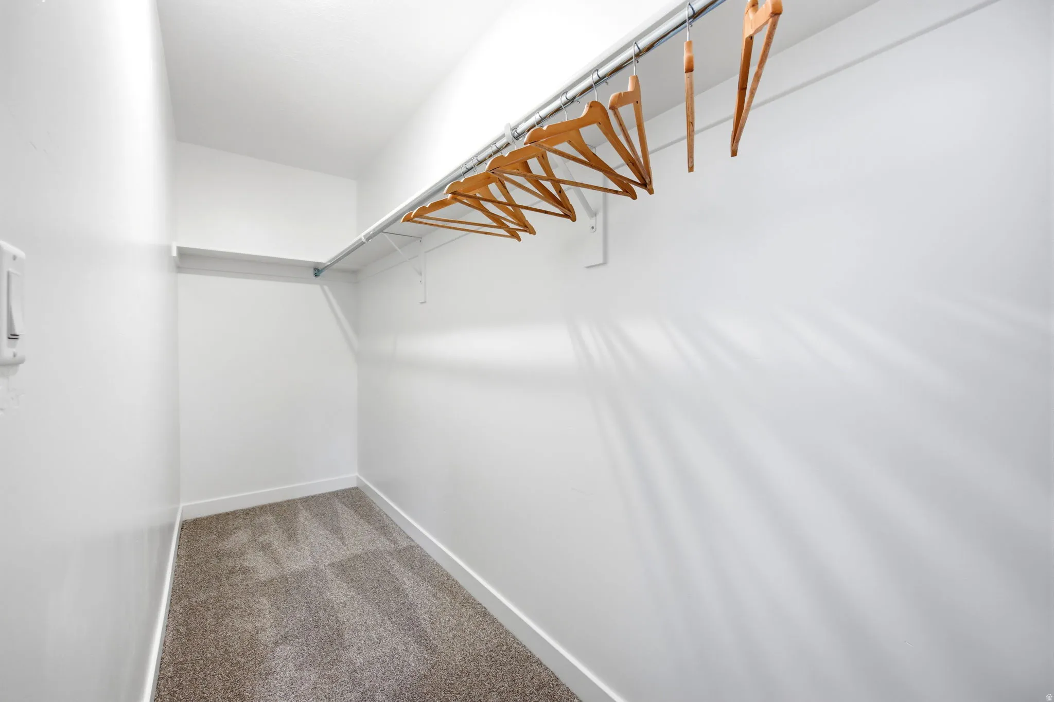 Spacious walk-in closet featuring light gray carpet, white walls, and a built-in wire shelf with a hanging rod