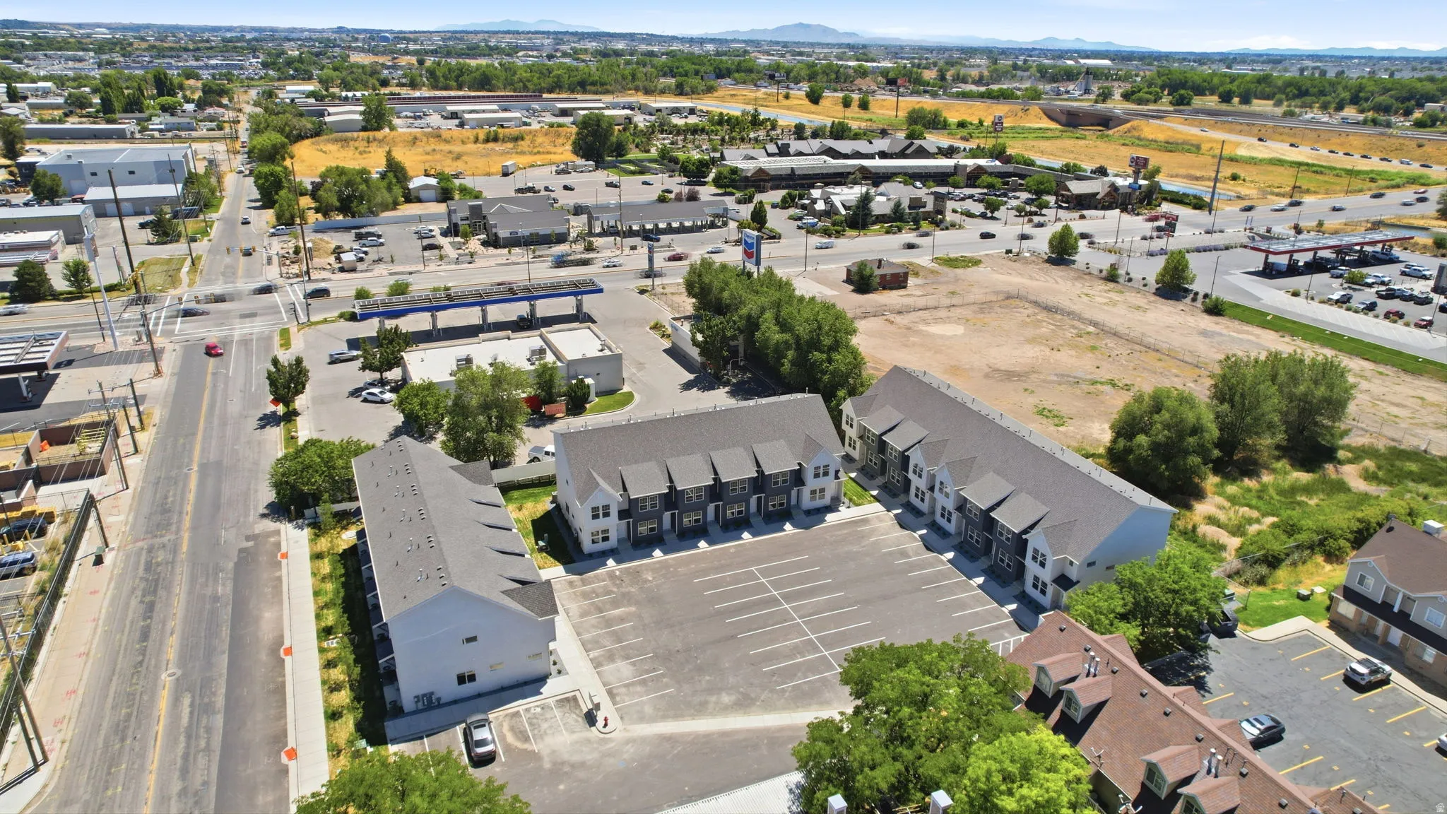 Modern townhome development featuring multiple units with varying exterior finishes, a dedicated asphalt parking area, and mature landscaping