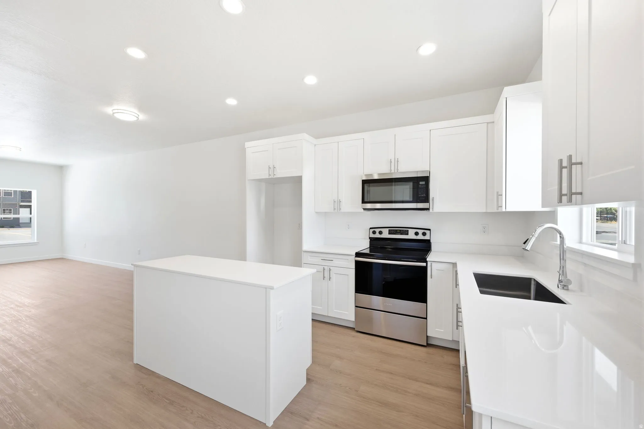 Open-concept kitchen featuring white shaker cabinetry, an island, stainless steel appliances, a black undermount sink, and wood-finish flooring