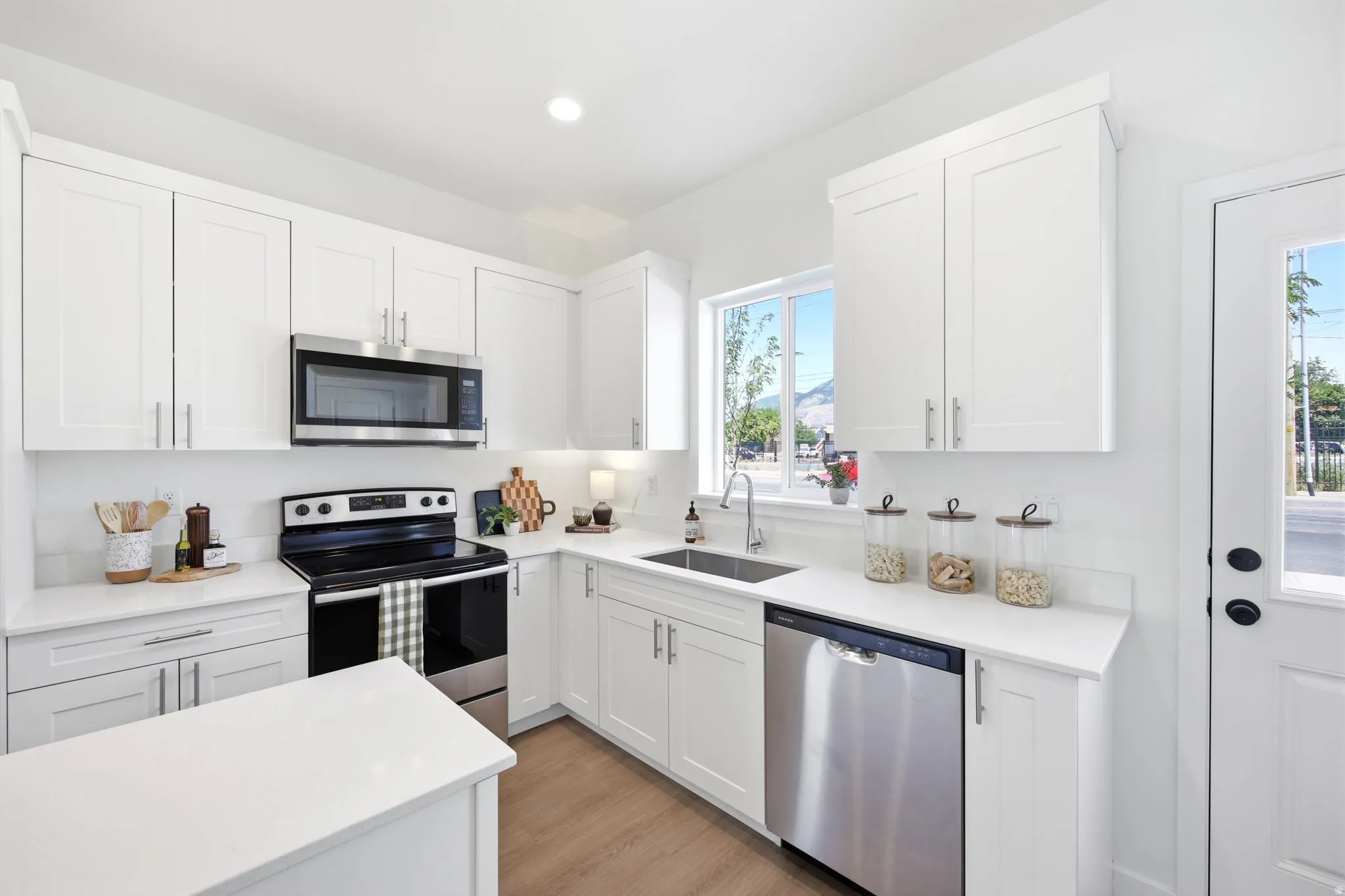 Modern kitchen featuring white shaker cabinetry, stainless steel appliances, a large window, and light wood-finish flooring