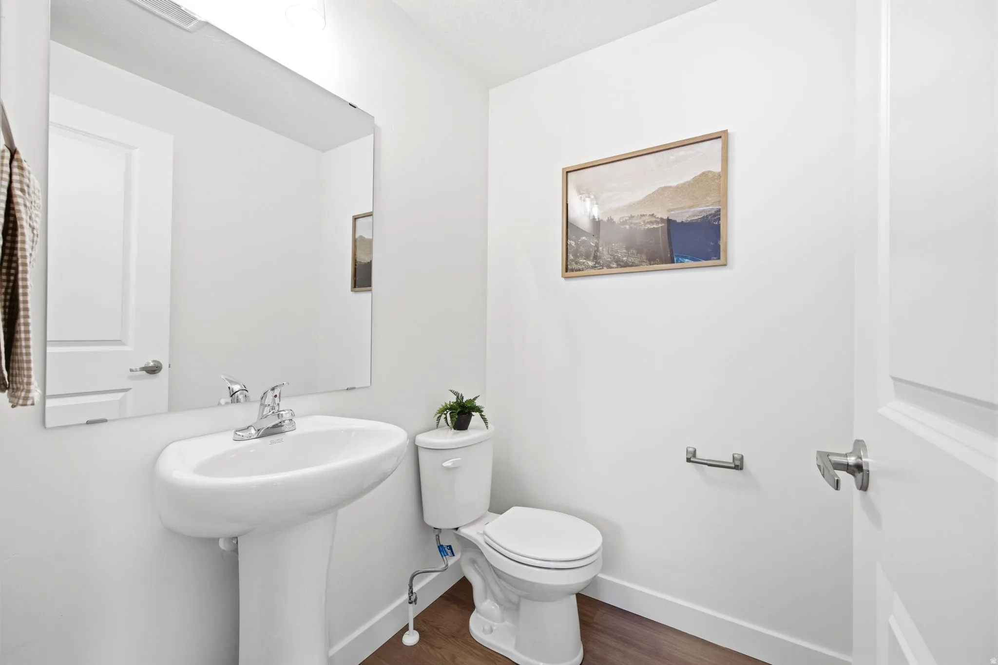 Pedestal sink with chrome faucet, large frameless mirror, and wood-finish flooring