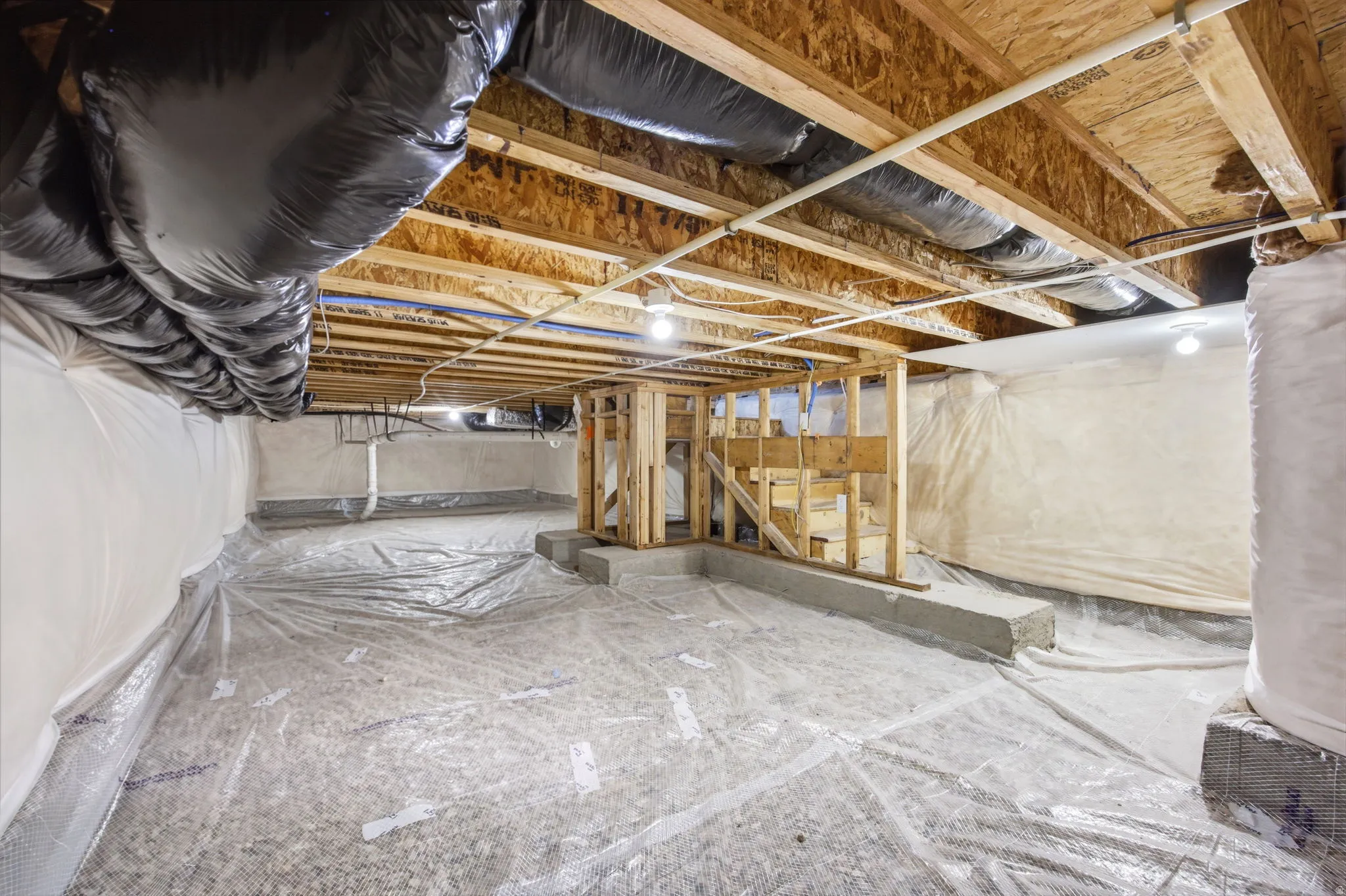 Unfinished crawlspace featuring exposed wood joists and subflooring, insulated walls and a partial wood-framed structure