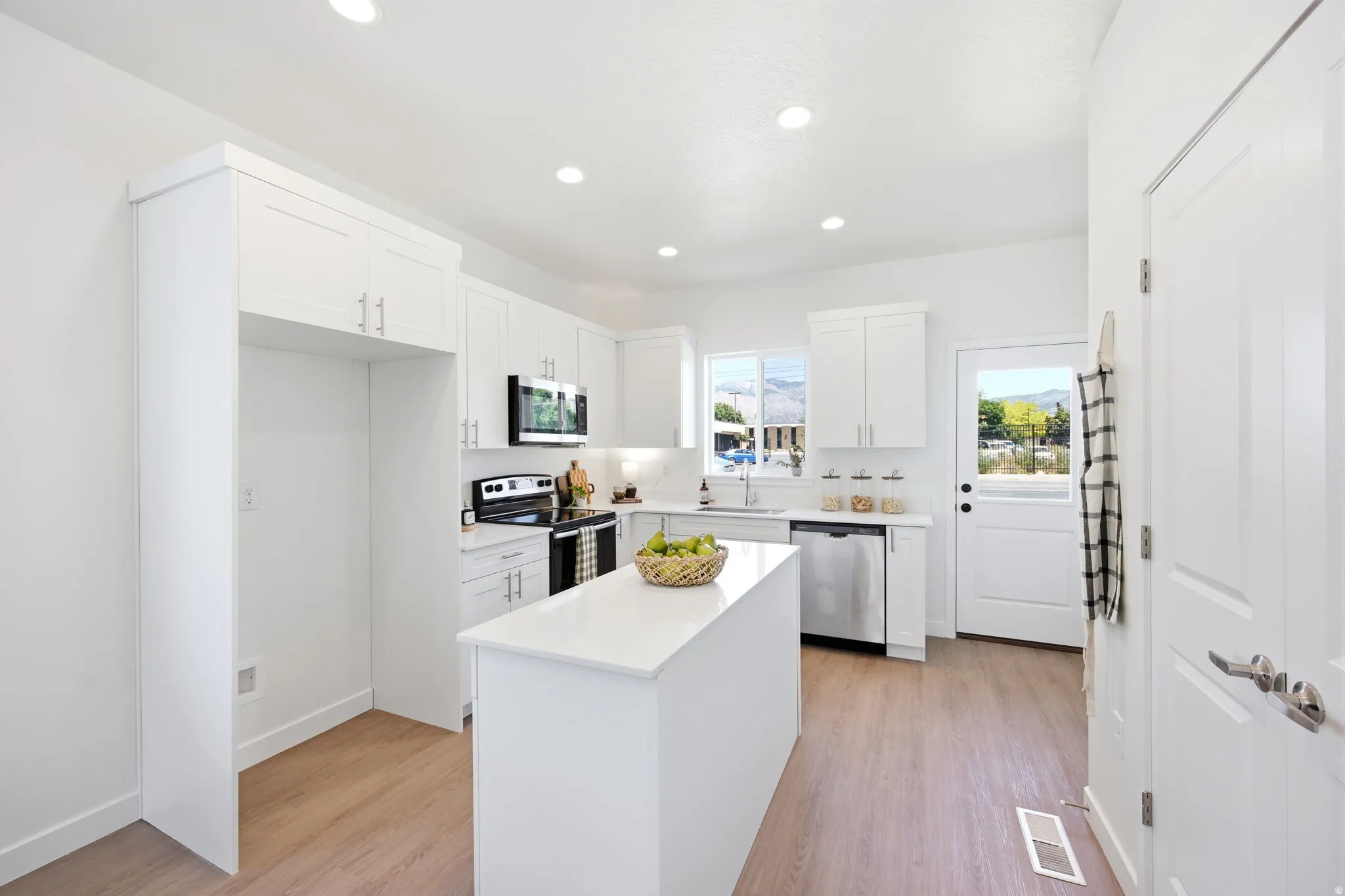 Contemporary kitchen featuring a central island, white cabinetry with brushed nickel hardware, stainless steel appliances, and light wood-finish flooring
