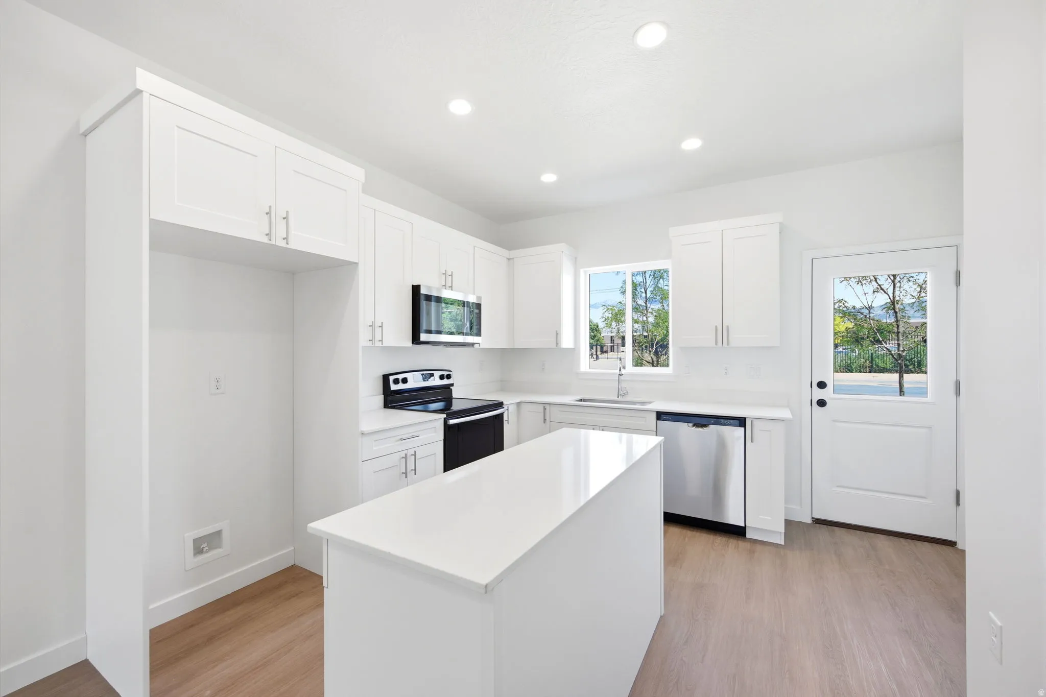 Modern kitchen featuring an island, white shaker cabinetry, stainless steel appliances, and wood-finish flooring