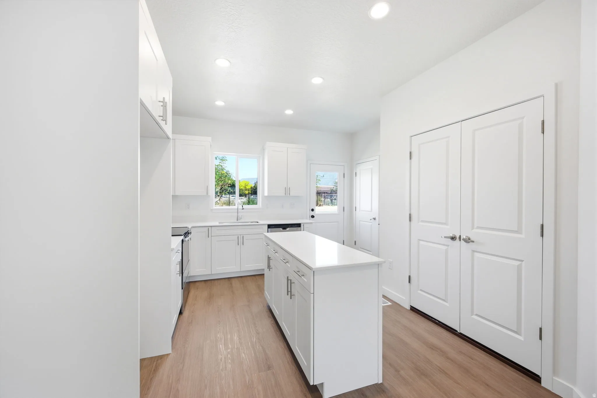 Bright kitchen featuring white cabinetry, a center island with a white countertop, wood-finish flooring, recessed lighting, and a double-door pantry