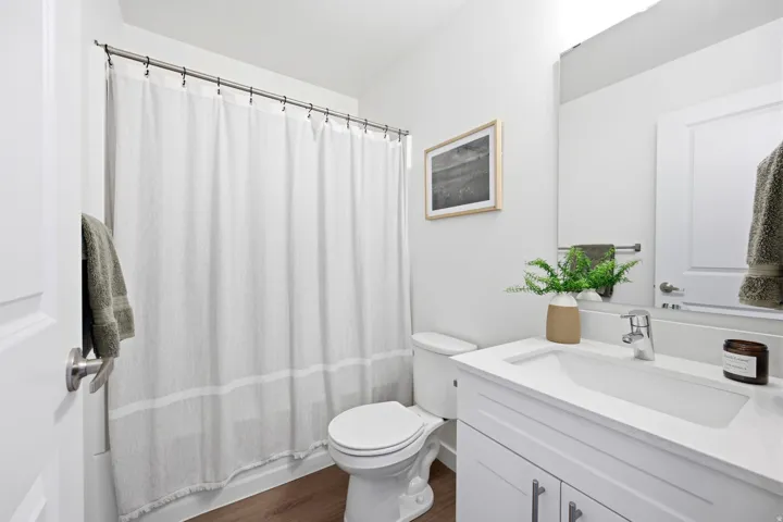 Bathroom featuring a white vanity with integrated sink, chrome faucet, wall-mounted mirror, and wood-finish flooring