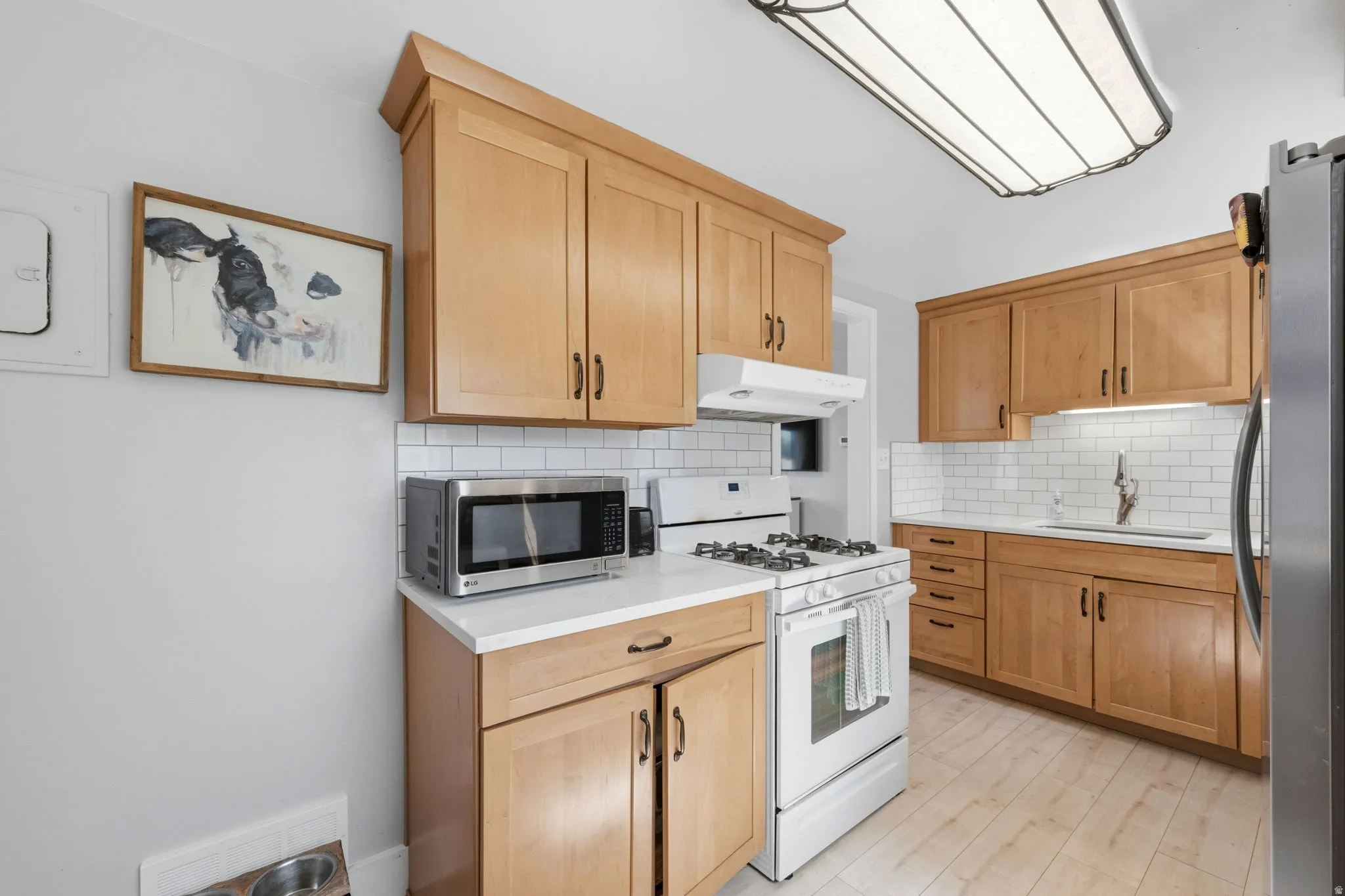 Light-toned wood cabinetry with contemporary hardware, white subway tile backsplash, and white countertops