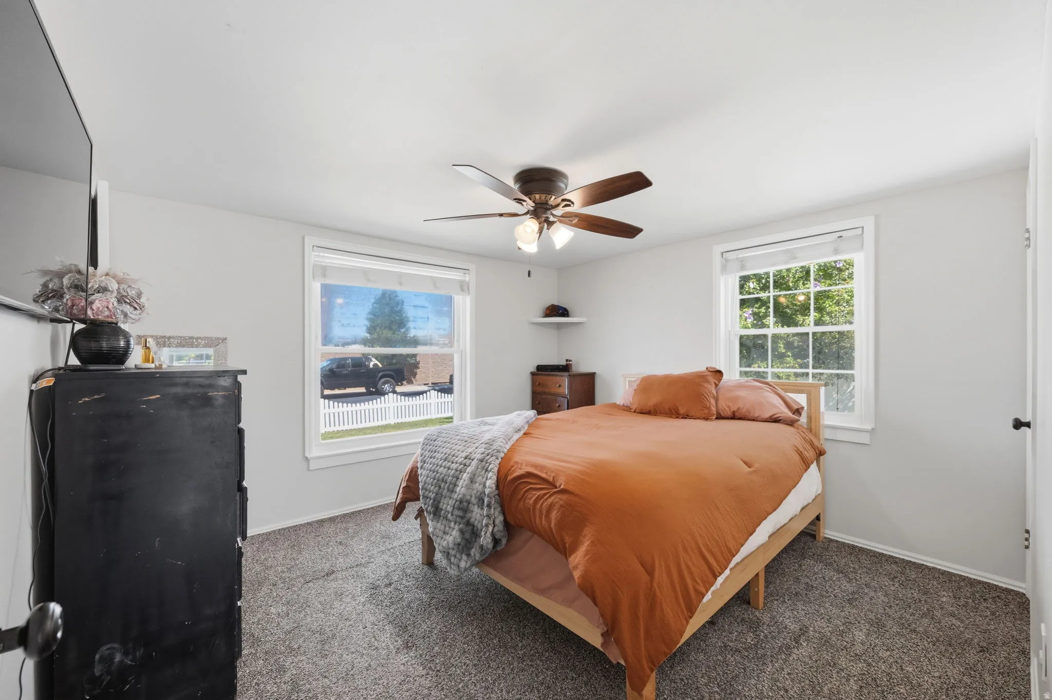 Carpeted room with a ceiling fan featuring a light fixture, two windows with white trim, and light gray walls