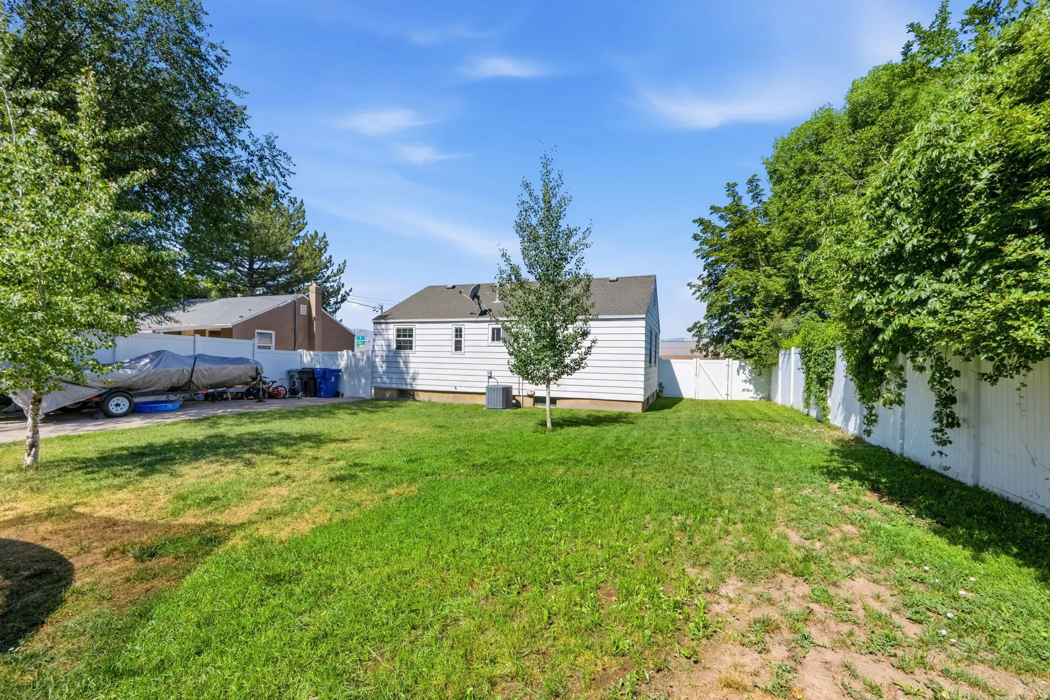 Expansive rear yard featuring green lawn, mature trees, and white privacy fencing