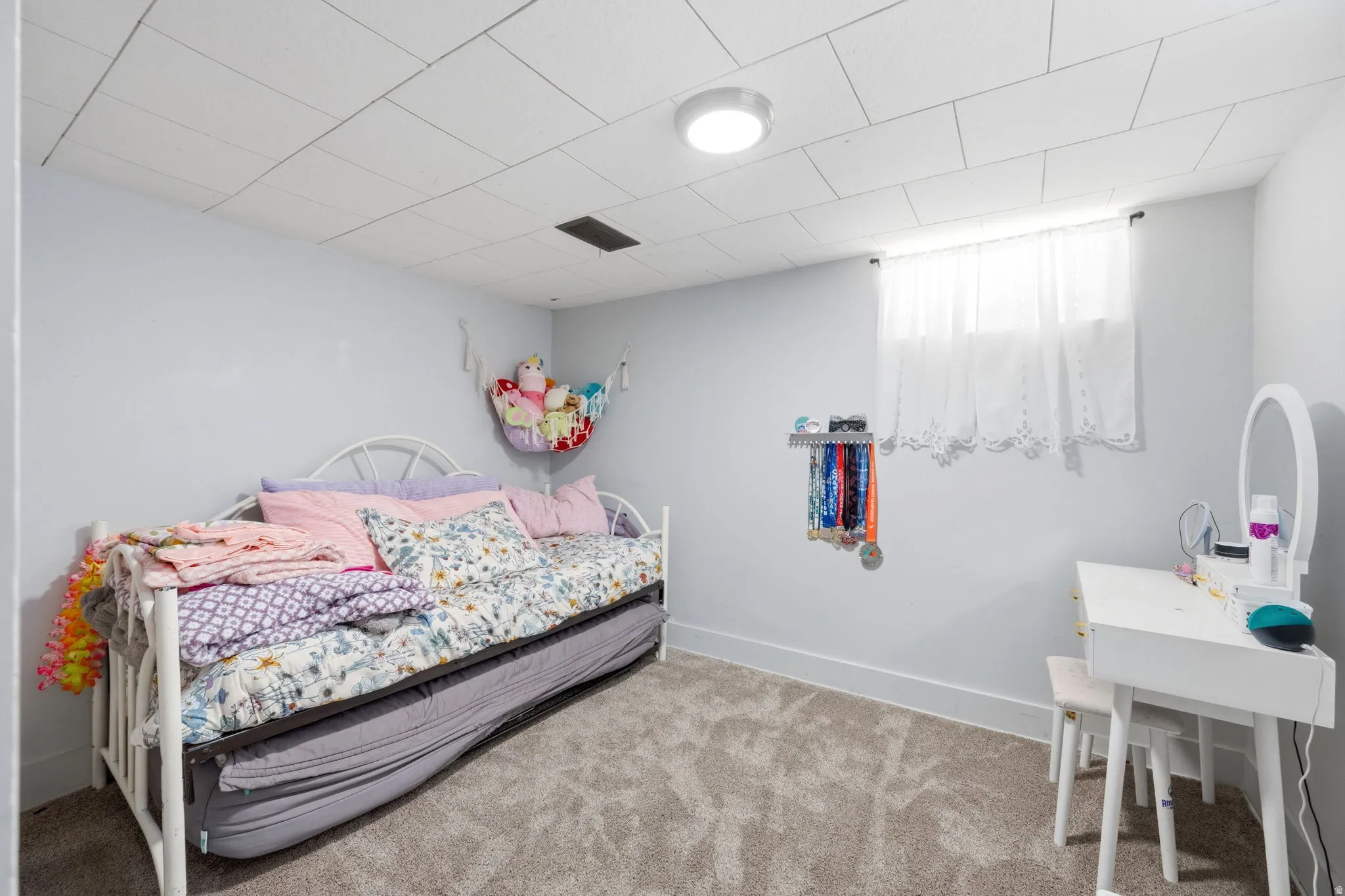 Carpeted room featuring a drop ceiling with recessed lighting, light-toned walls, and a window with white curtains