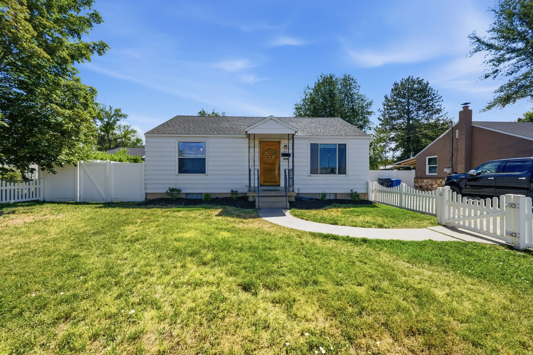 White picket fence surrounding the property, a curved concrete walkway, and a landscaped front yard with dark mulch