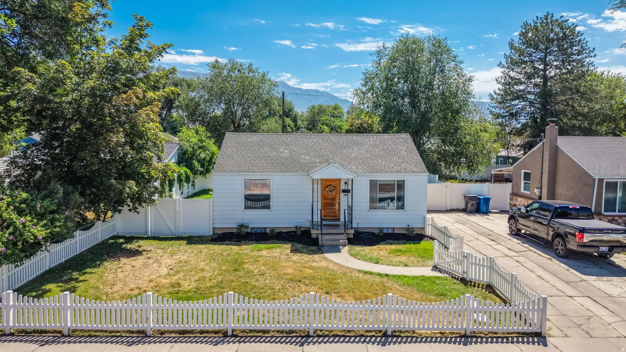 Charming single-story residence featuring a white picket fence, white siding, and a wooden front door