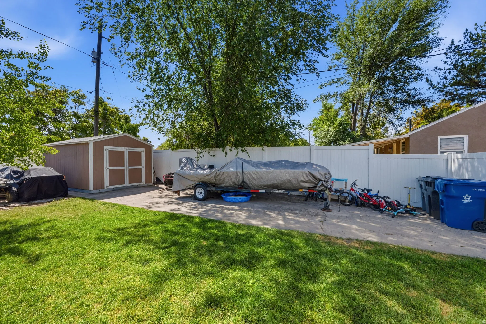 Spacious backyard featuring a manicured lawn, a detached storage shed, and a white privacy fence