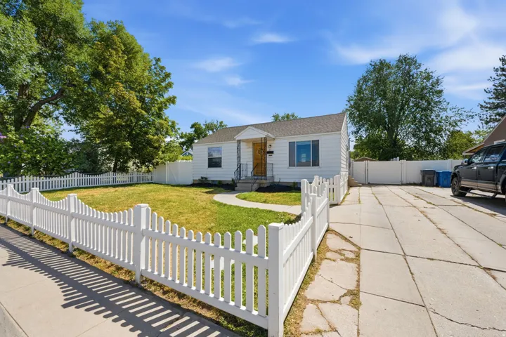 White picket fence enclosing a front lawn with mature trees and a concrete walkway leading to the front door