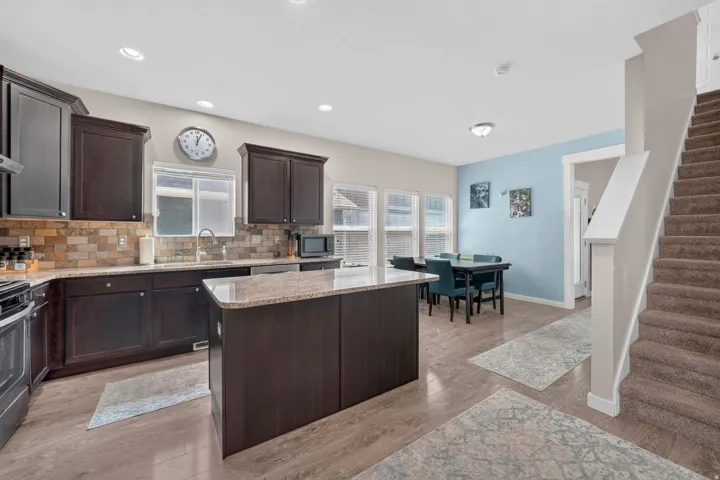 Open-concept kitchen and dining area featuring dark wood cabinetry, a granite-topped island, and stainless steel appliances