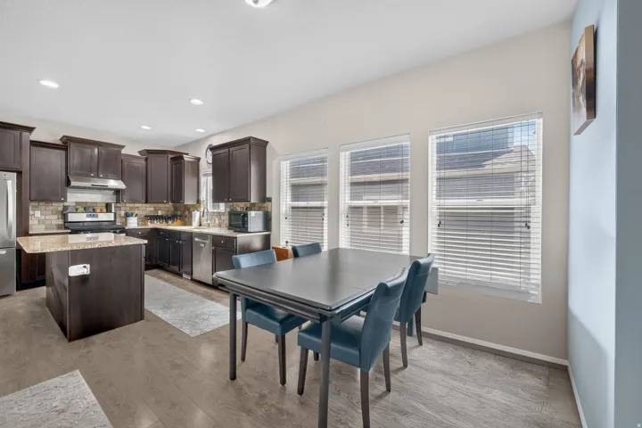 Kitchen and dining area featuring dark wood cabinetry, stainless steel appliances, a central island with a stone-finish countertop, and wood-finish flooring