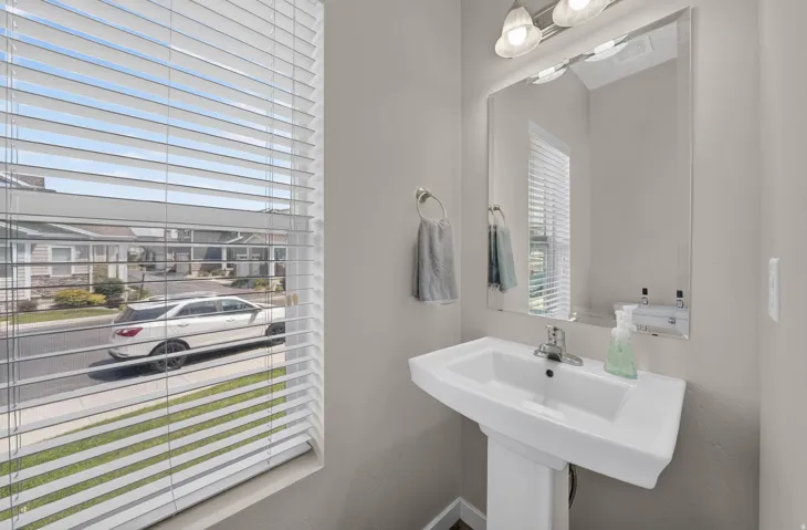 Pedestal sink with chrome faucet, large frameless mirror, and overhead vanity lighting