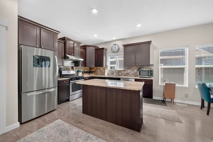 Kitchen featuring wood-finish flooring, dark wood cabinetry, a central island with a light-toned countertop, and stainless steel appliances