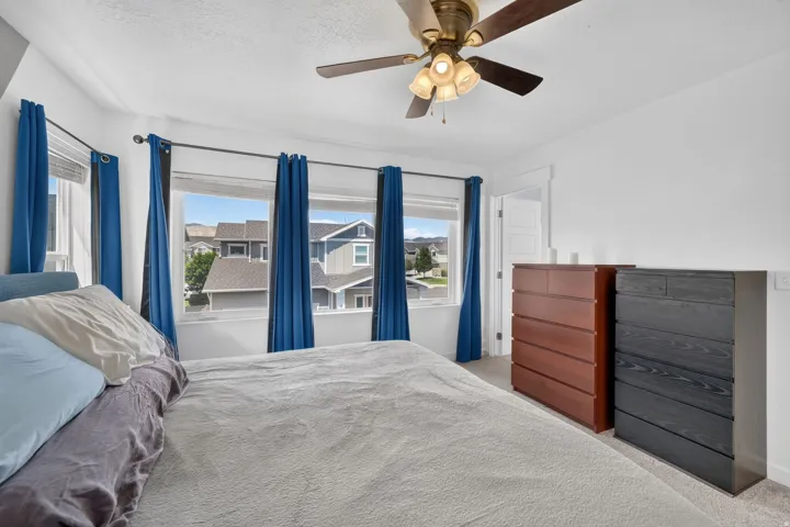 Bedroom featuring multiple windows, a ceiling fan with integrated lighting, and neutral carpeting