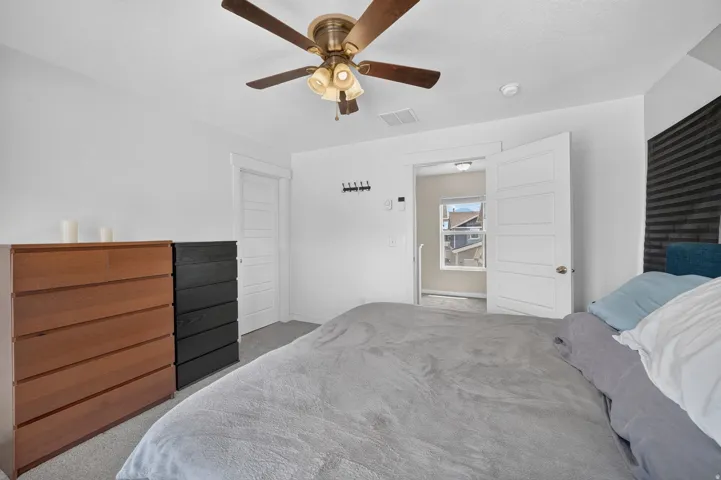 Carpeted room with a ceiling fan featuring a brass-tone base and wood-finish blades, white walls, and a white paneled door