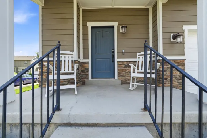 Inviting front porch featuring a blue entry door, complementary stone accent siding, and durable composite siding