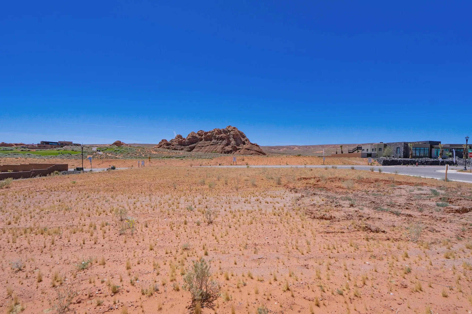 Expansive desert landscape featuring a clear blue sky, distant rock formations, and paved roadways