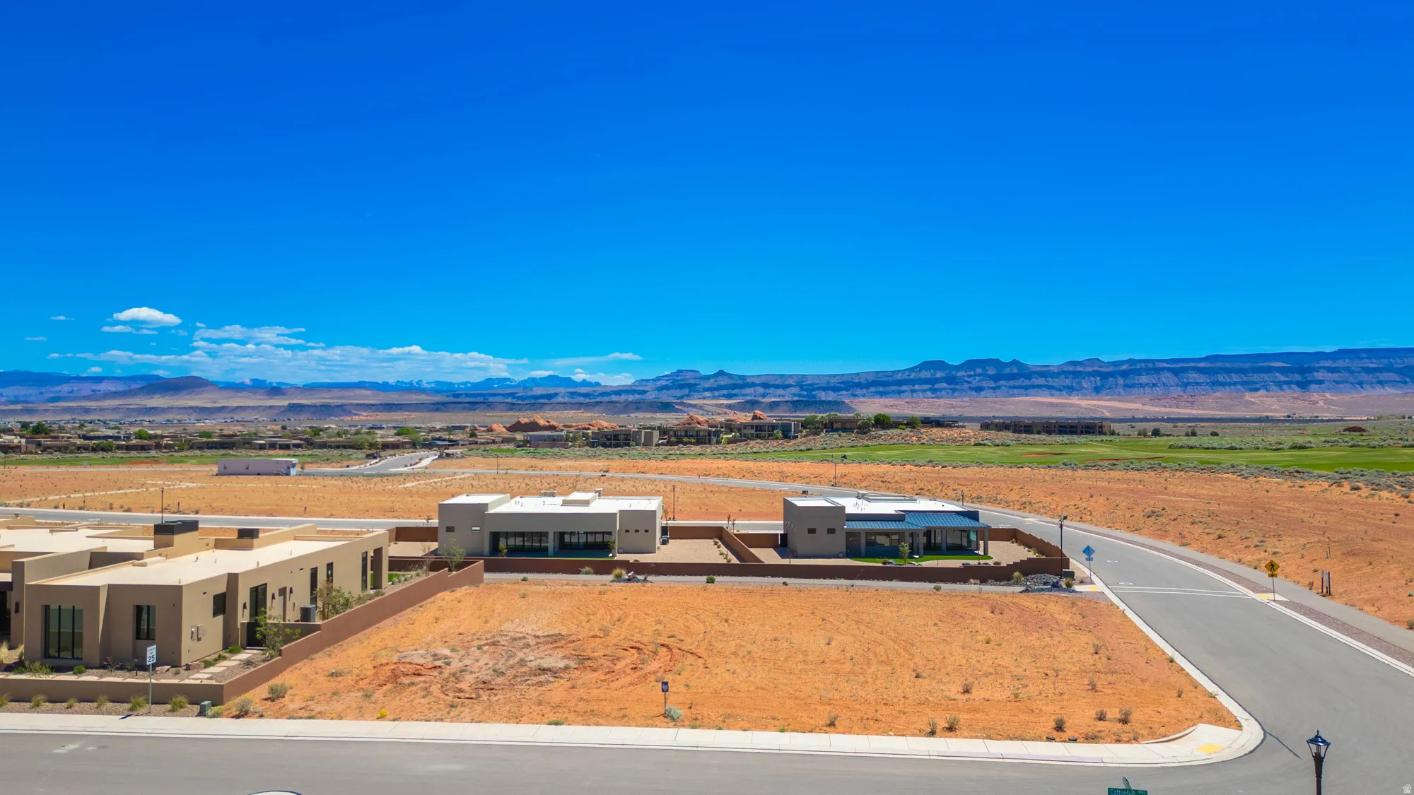 Modern desert landscape featuring a paved road, developing residential properties, and distant mountains
