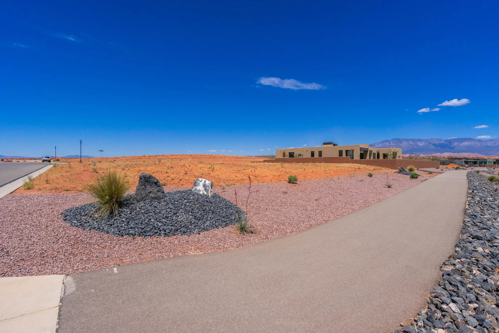 Expansive undeveloped land parcel with a paved pathway, desert landscaping, and distant mountain backdrop