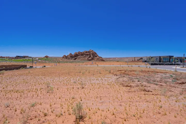 Expansive desert landscape featuring a clear blue sky, distant rock formations, and paved roadways
