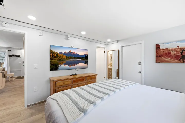 Bedroom featuring light wood-finish flooring, recessed ceiling lighting, and a wall-mounted flat-screen television above a wooden dresser