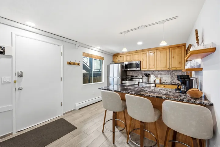 Kitchen featuring wood cabinetry, stainless steel appliances, a dark countertop, and a stone-finish backsplash